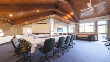 Uma sala de conferências com uma mesa comprida, cadeiras pretas, vigas de madeira no teto e grandes janelas.