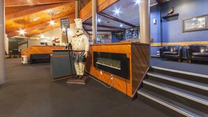 Interior de restaurante con techo de madera, una estatua de chef, chimenea y asientos de cuero.