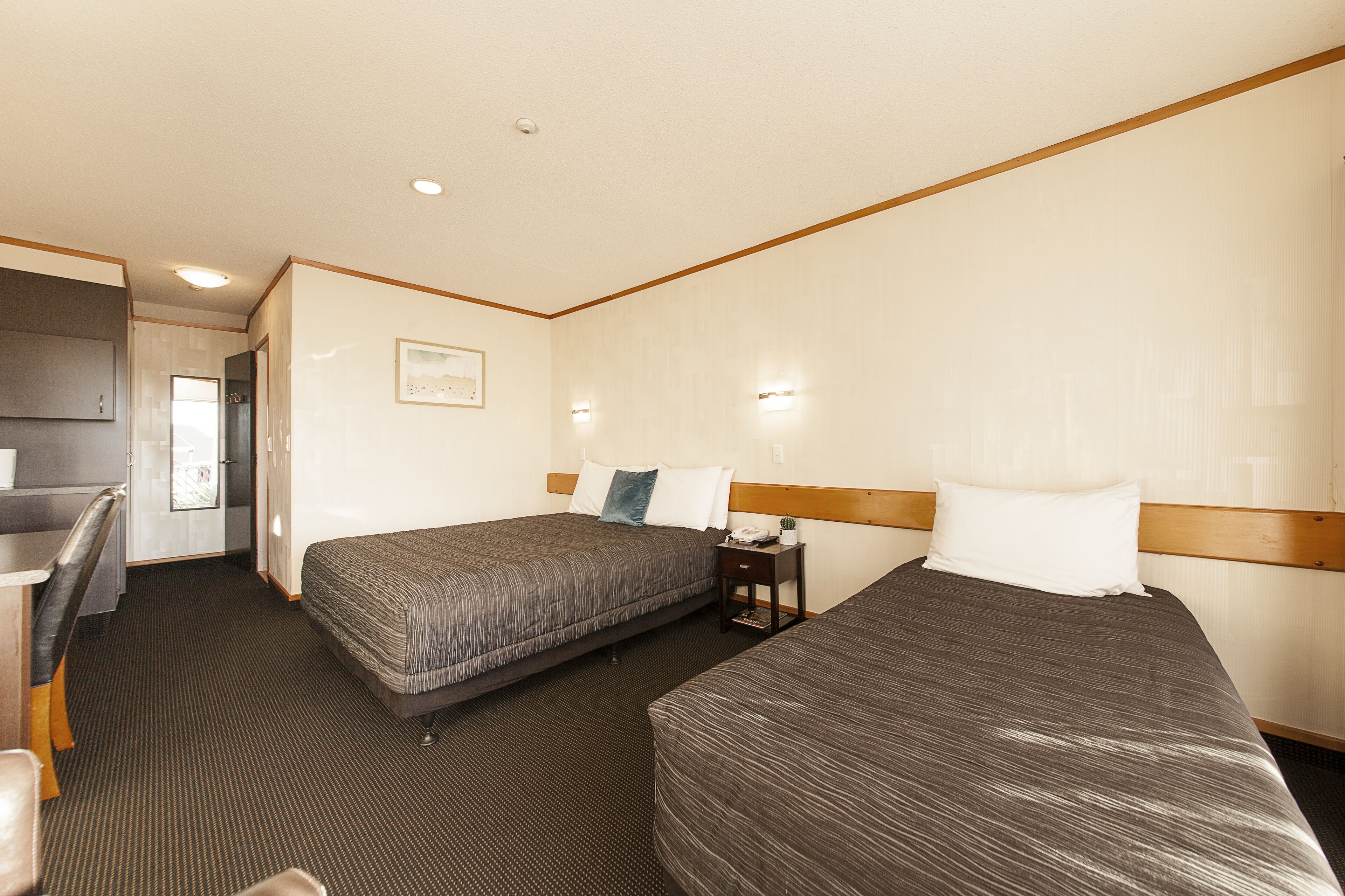 A hotel room with two beds, a desk, and a small table.