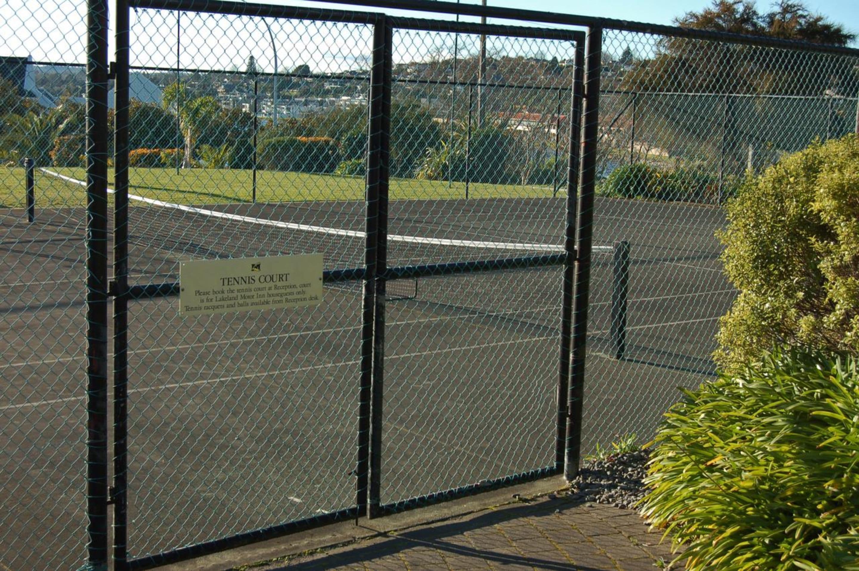 A tennis court enclosed by a chain-link fence with a sign indicating it is a tennis court.