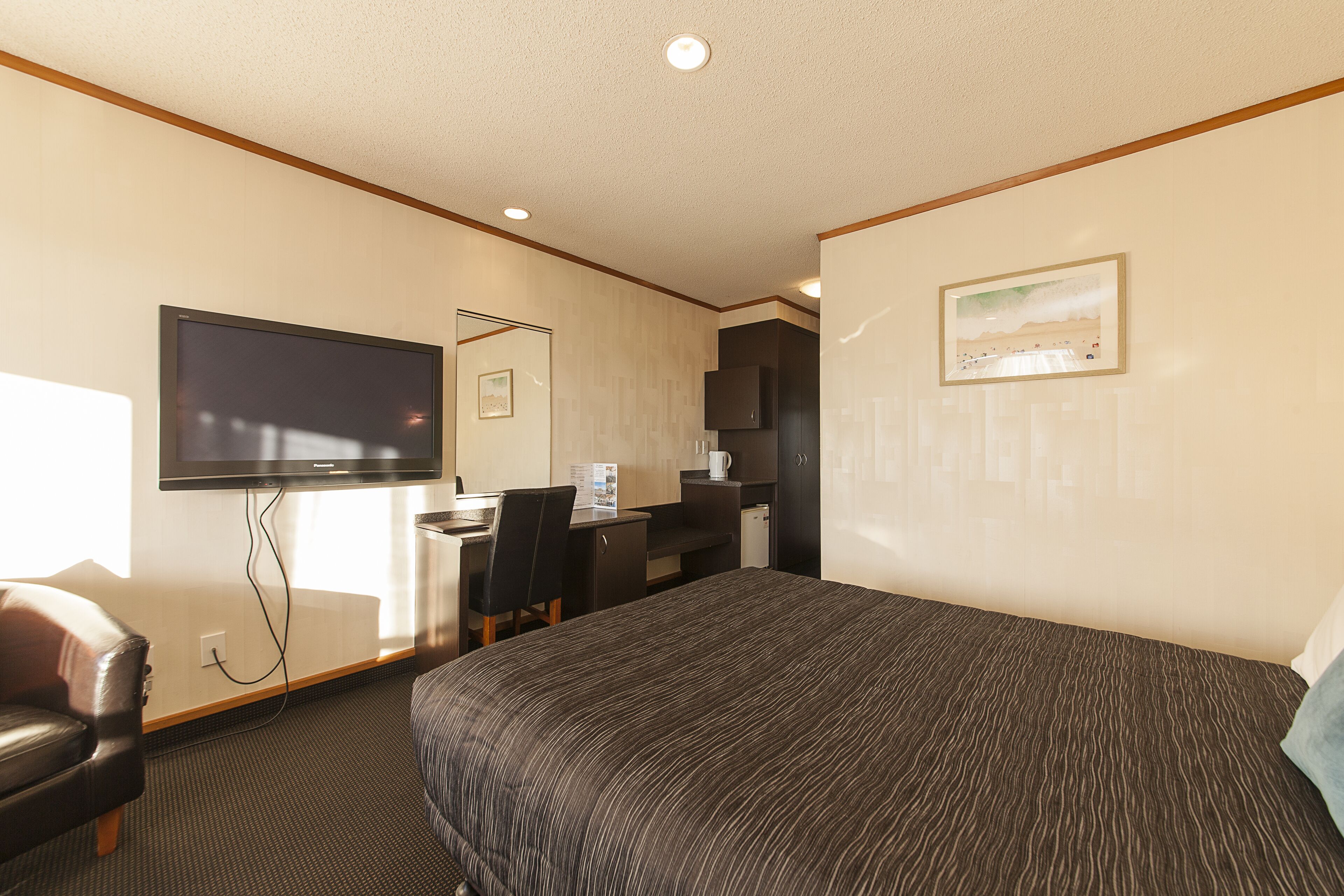 Una habitación de hotel con cama, escritorio, silla, televisión y un cuadro en la pared.