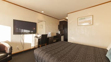 Una habitación de hotel con cama, escritorio, silla, televisión y un cuadro en la pared.