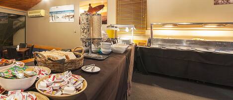 A buffet setup with various food items, a fruit bowl, and a juice dispenser.