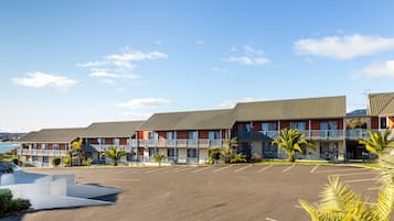 A motel with multiple-story buildings, a parking lot, and a view of the ocean.