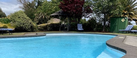 Uma piscina com área pavimentada ao redor, espreguiçadeiras e um gazebo.