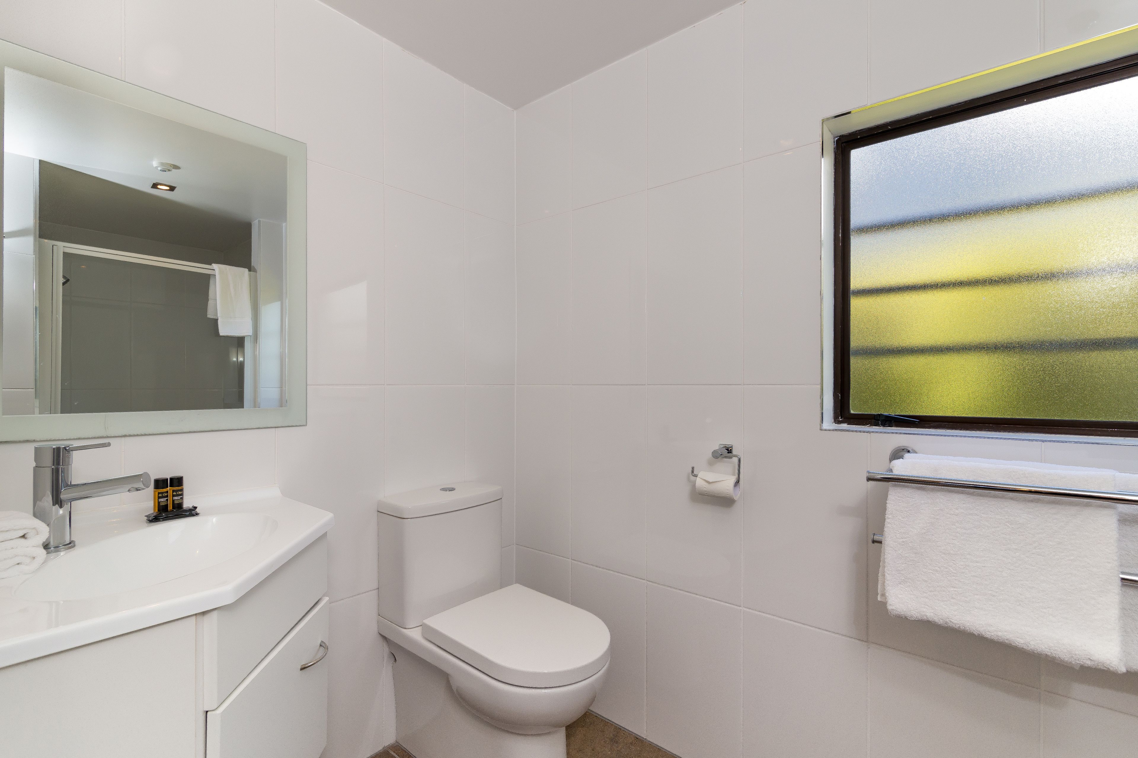 A modern bathroom with a white sink, toilet, and a large mirror.