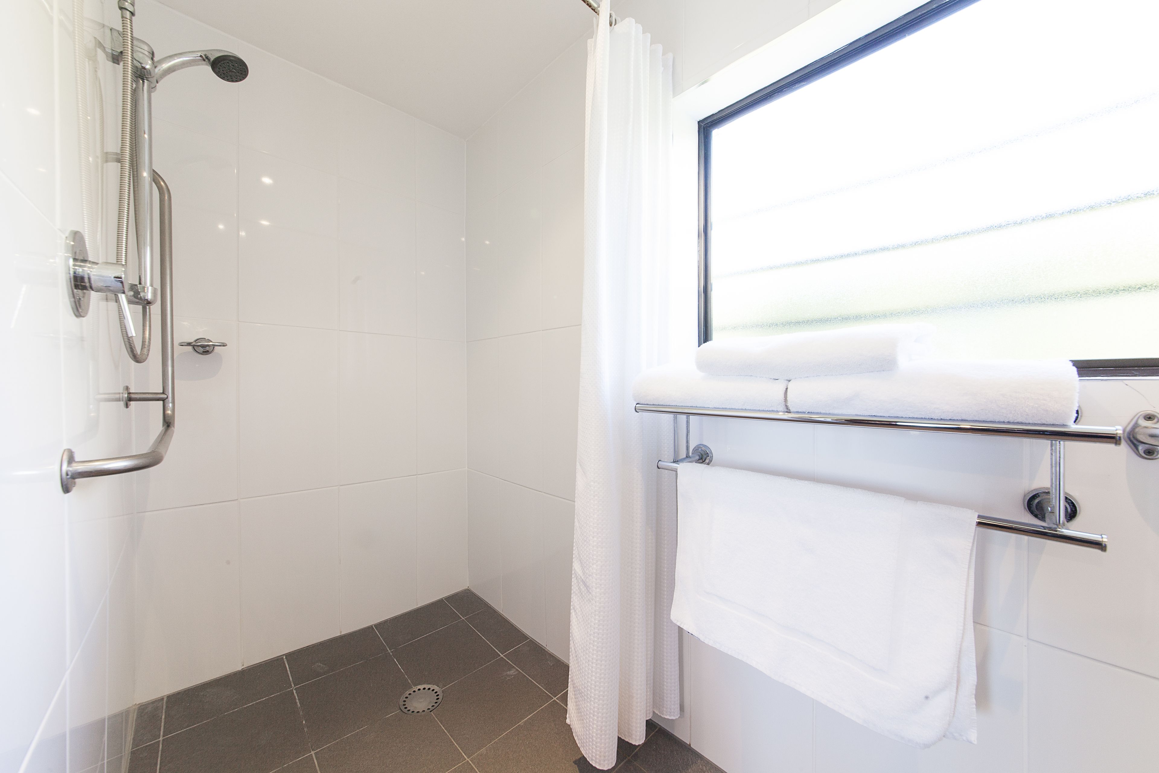 A shower area with a handheld showerhead, a glass door, and a towel rack with two towels.