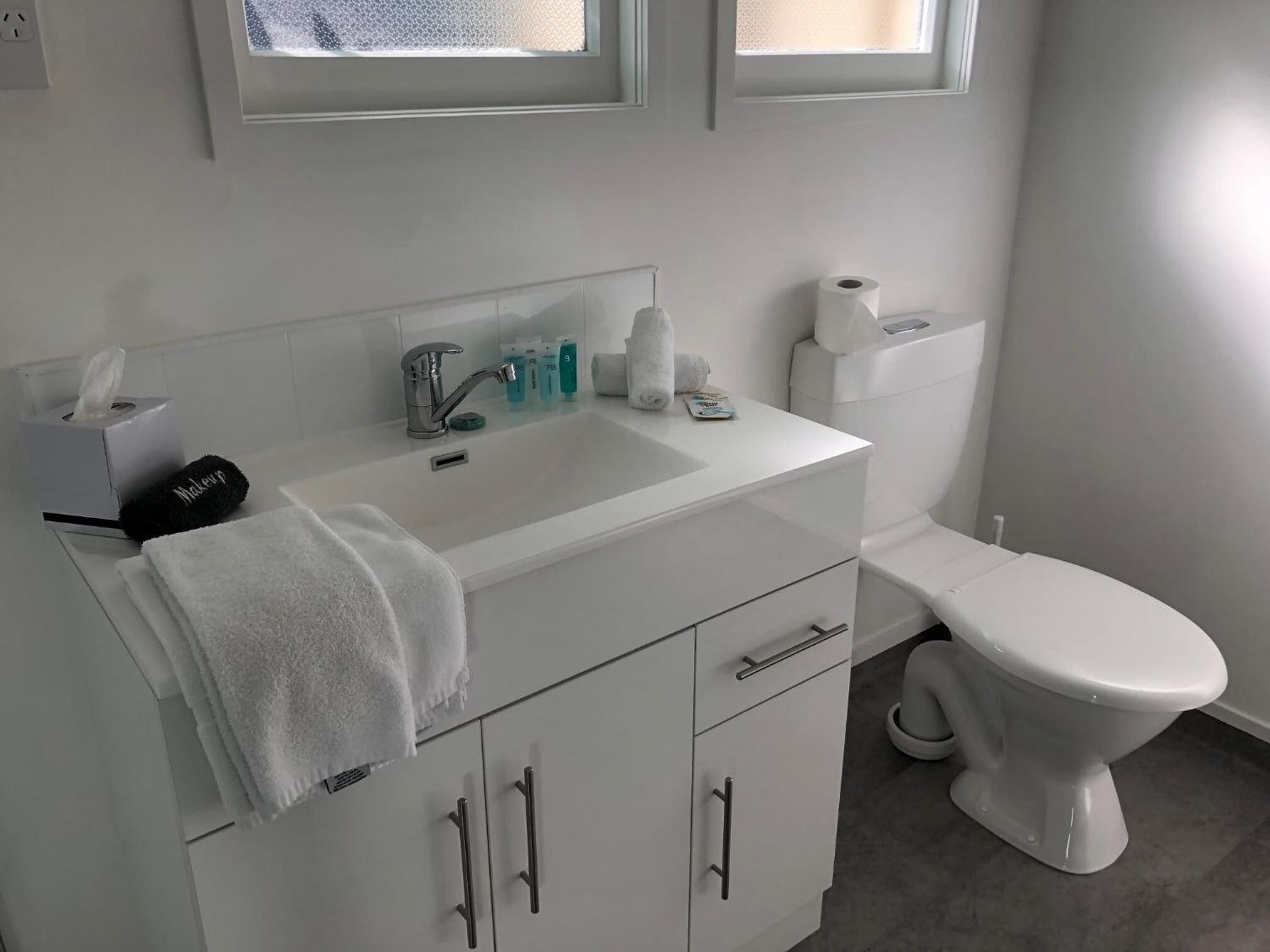 Un baño moderno con lavamanos blanco, inodoro y tocador con armarios.