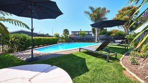 A backyard with a swimming pool, two lounge chairs, and umbrellas. - Cobblestone Court Motel – Wenzel Motels (Tauranga)