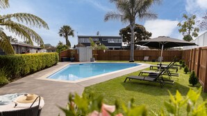 A backyard with a swimming pool, lounge chairs, and a hot tub. - Cobblestone Court Motel – Wenzel Motels (Tauranga)