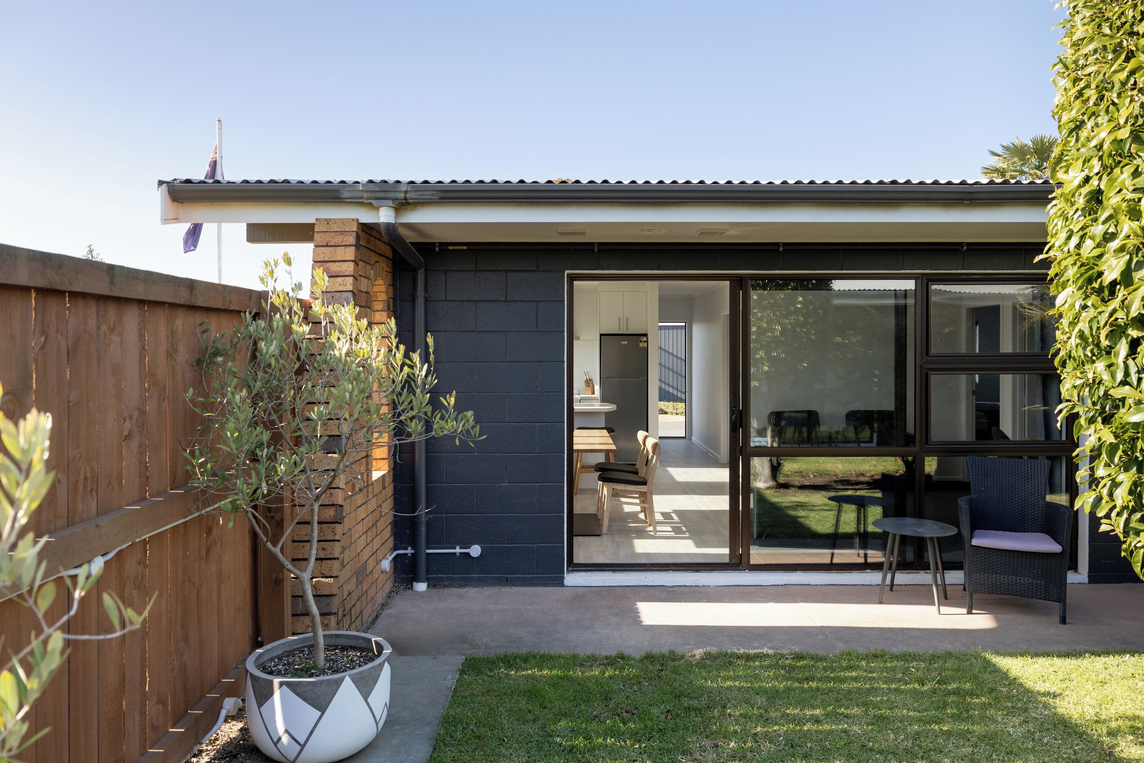 A modern house with a patio area featuring a small table and chairs, a potted plant, and a wooden fence.