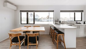 A modern kitchen with a large island, bar stools, and a dining area with wooden chairs. - Cobblestone Court Motel – Wenzel Motels (Tauranga)