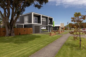 Um motel moderno de dois andares, com telhado plano, grandes janelas e uma placa verde visível.