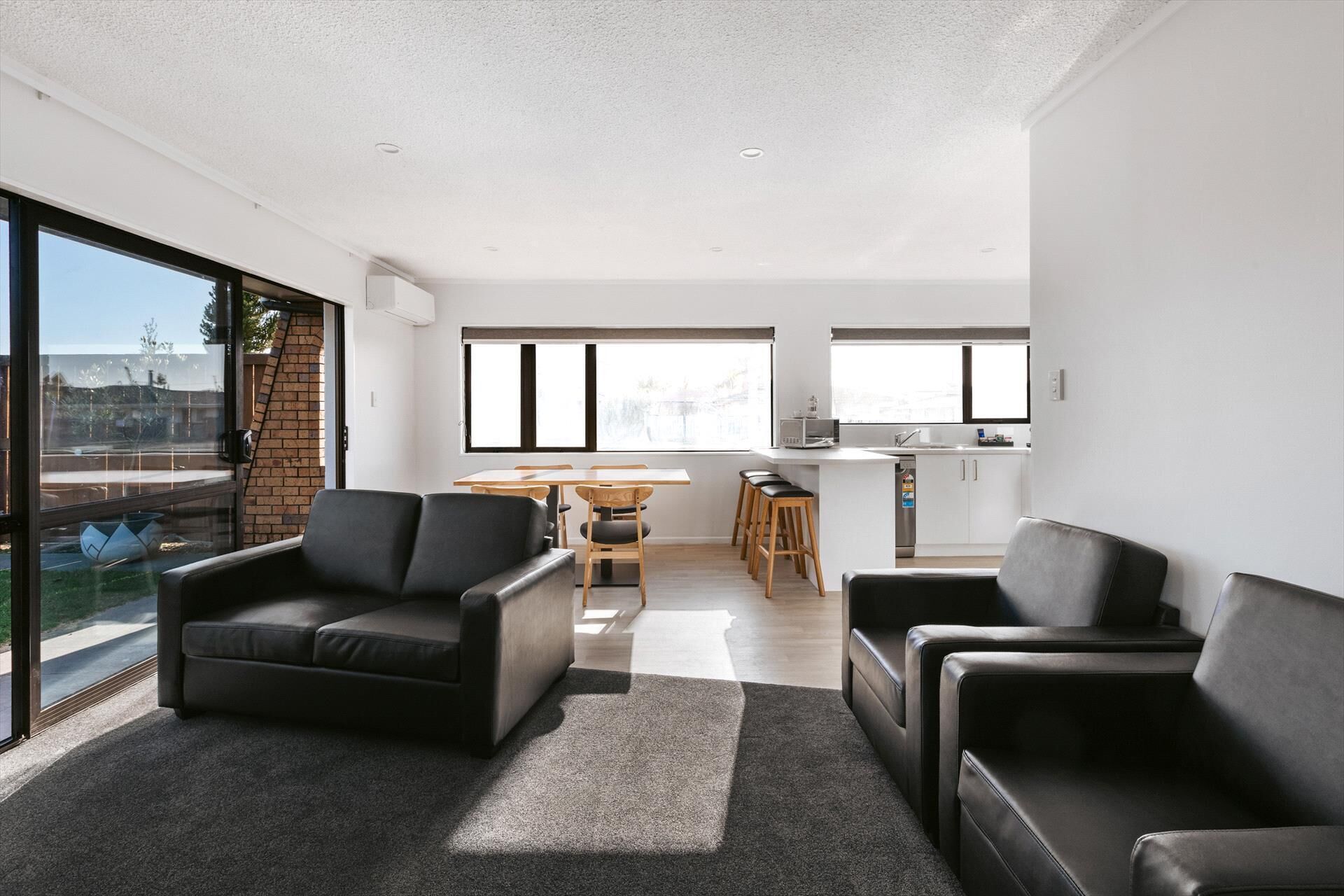 A modern living room with a sofa, a dining area with a table and chairs, and a kitchen area with a sink and countertop.