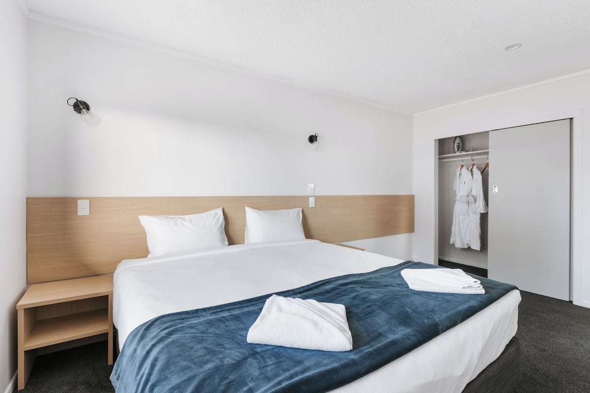 Ein Hotelzimmer mit einem großen Bett, einem Holzkopfende, einem Nachttisch, einem Kleiderschrank und einem Spiegel.