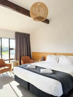 A hotel room with a large bed, a wooden headboard, a wicker ceiling light, a window with curtains, and a view of the outside.