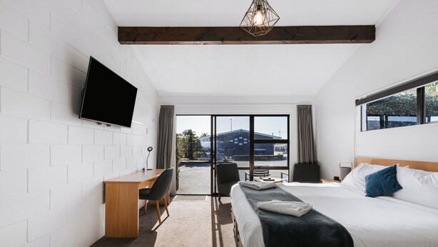 A modern hotel room with a bed, desk, and TV. - Cobblestone Court Motel – Wenzel Motels (Tauranga)