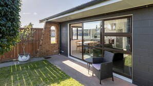 A patio with a glass door leading to an outdoor dining area, a brick wall, and a small tree. - Cobblestone Court Motel – Wenzel Motels (Tauranga)