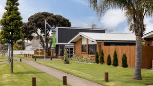 A modern building with a brick facade, a flat roof, and a well-maintained lawn with young trees and a pathway. - Cobblestone Court Motel – Wenzel Motels (Tauranga)