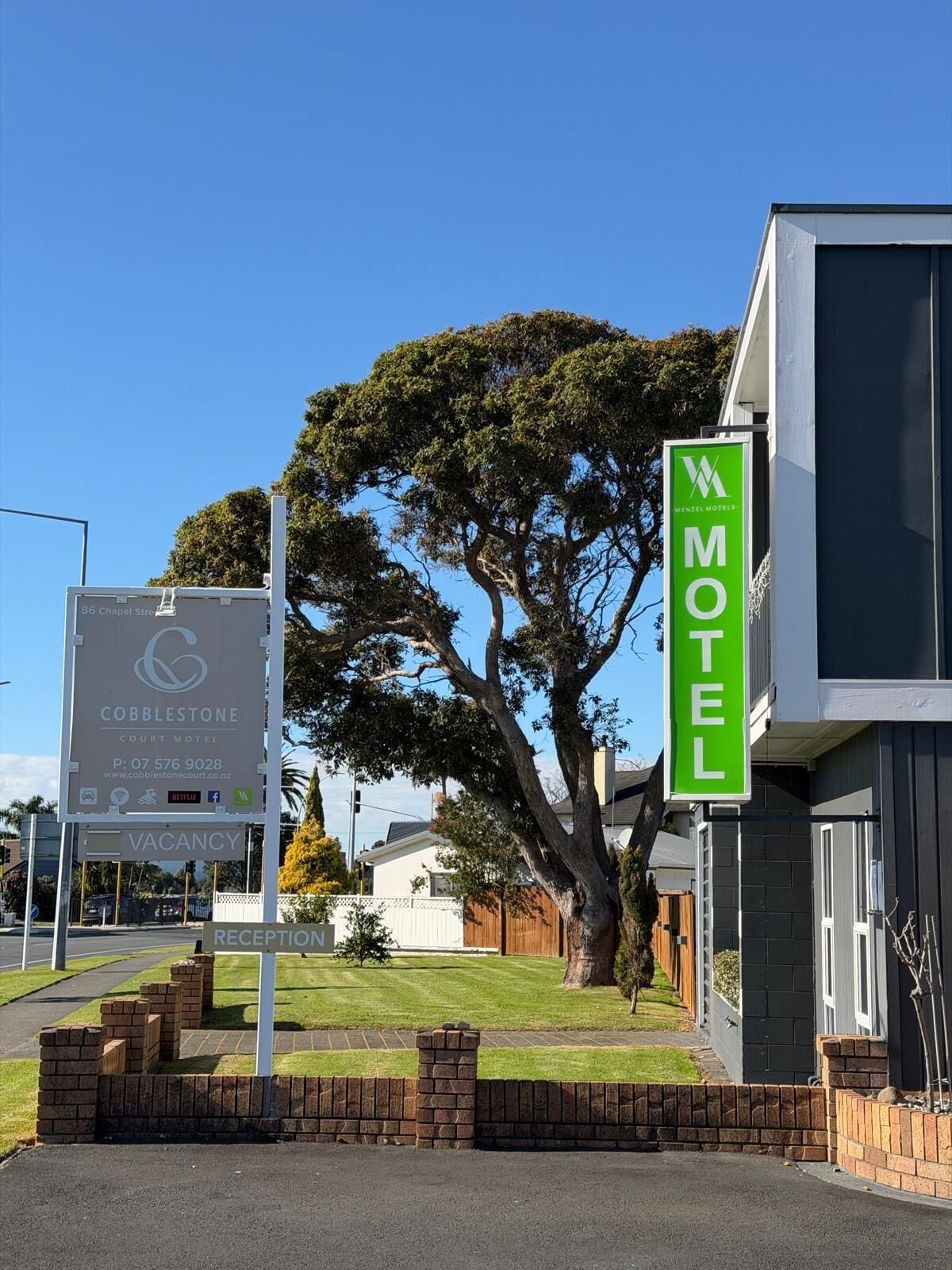 A Cobblestone Court Motel sign with a reception area and a large tree in the background.