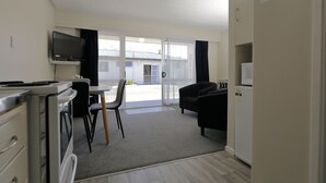 En kompakt opholdsstue med tekøkken, spiseplads, sofa og fjernsyn.