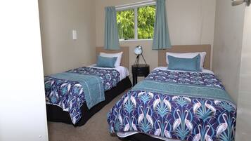 A bedroom with two beds, each with a patterned bedspread, a nightstand with a lamp, and a window with curtains.