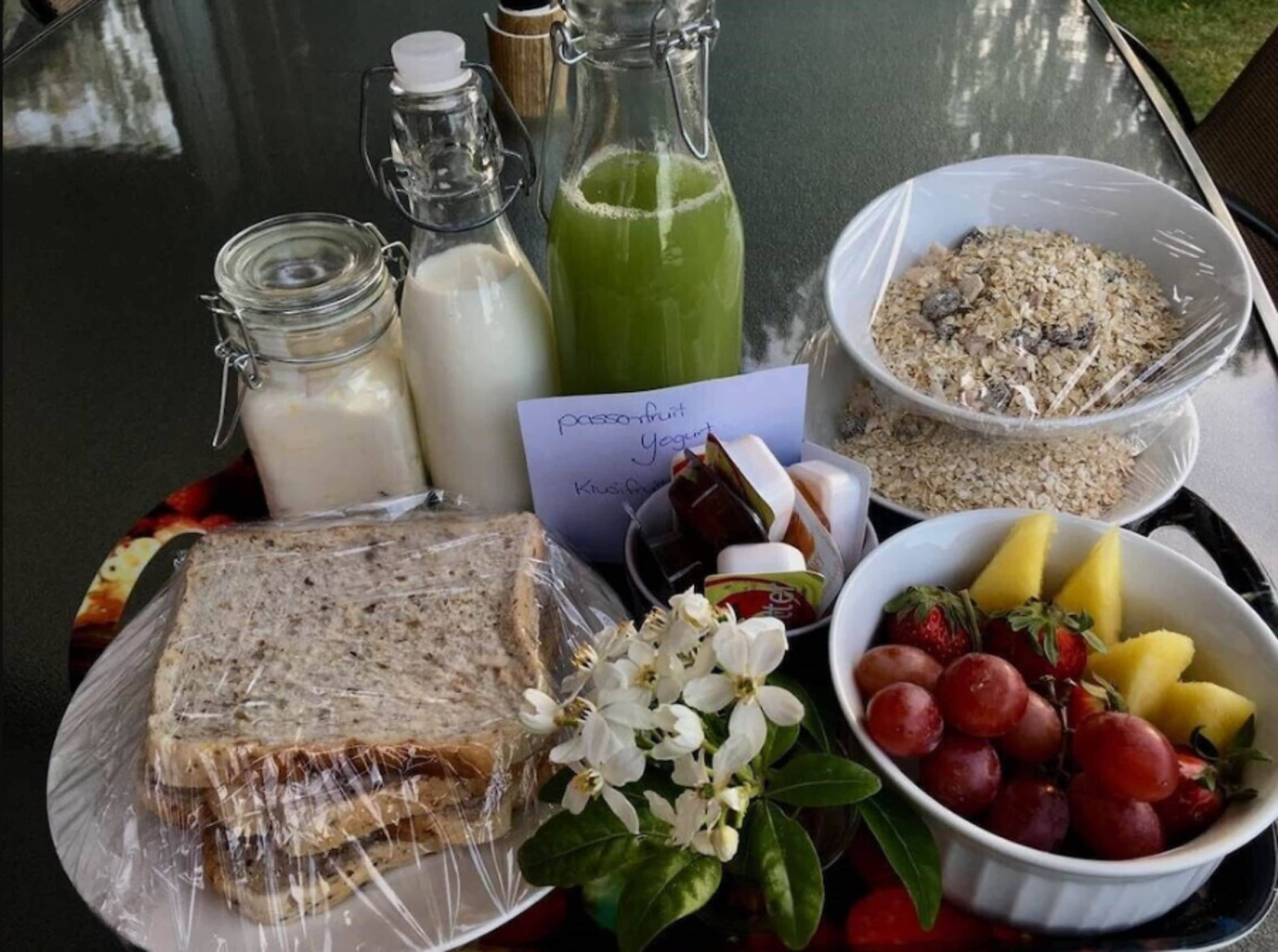A table with food items including bread, yogurt, green juice, granola, and fruits.