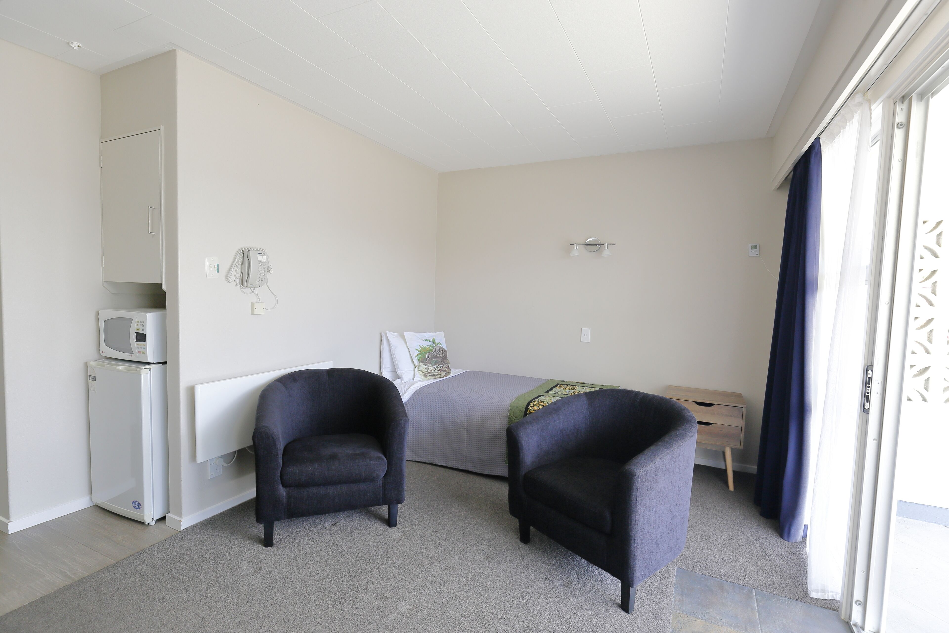 Une chambre à coucher comprenant un lit, deux fauteuils, un bureau, un four à micro-ondes et un petit réfrigérateur.