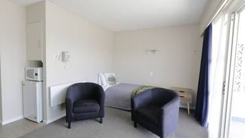 Un dormitorio con una cama, dos sillones, un escritorio, un microondas y un refrigerador pequeño.