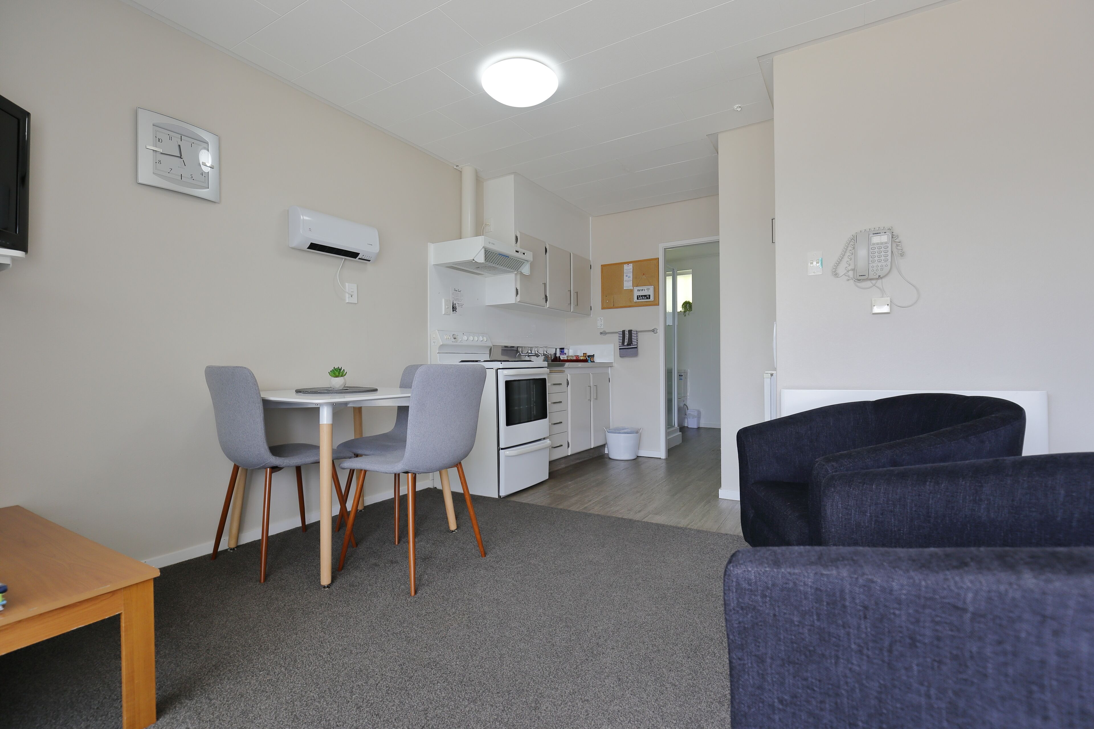 Een knus woongedeelte met een kitchenette, een eethoek met twee stoelen, een kleine tafel en een bank.