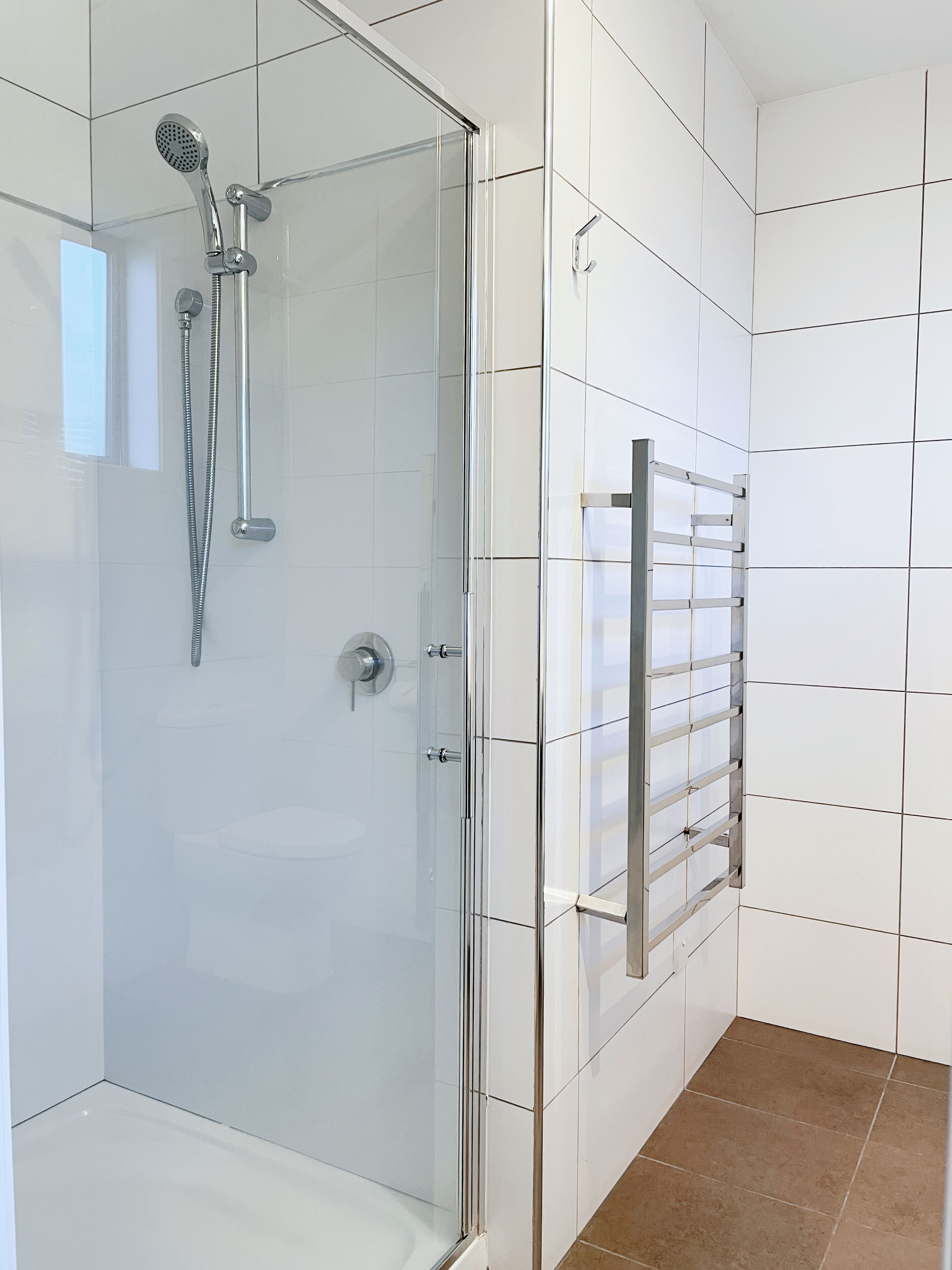 Une salle de bain moderne avec une douche à parois de verre, une pomme de douche chromée et un porte-serviettes fixé au mur.