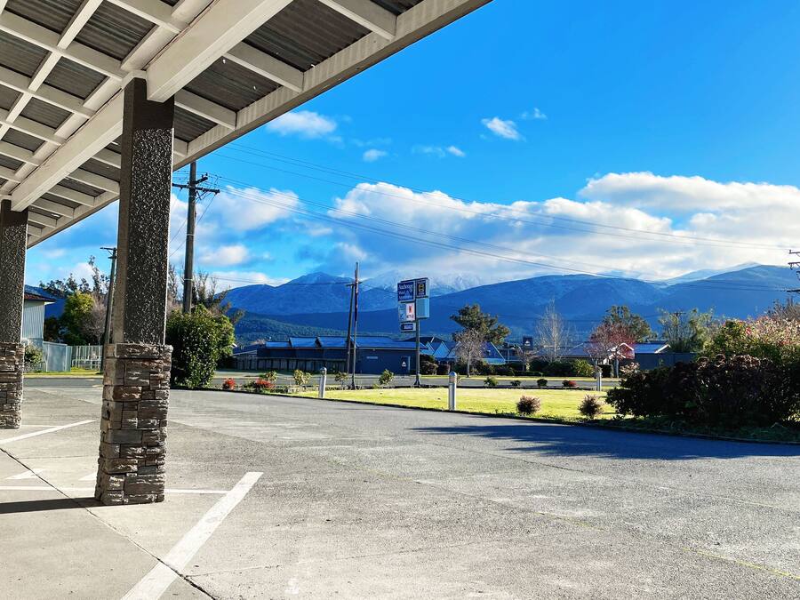 A parking area with a covered walkway, stone pillars, and a view of mountains in the background.