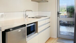 A modern kitchen with a built-in dishwasher, oven, and double sink. There is a window with a view of the outdoors. - Anchorage Motel Apartments (Te Anau)