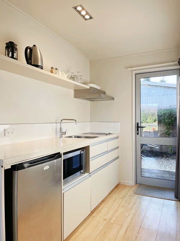 A modern kitchen with a built-in dishwasher, oven, and double sink. There is a window with a view of the outdoors. - Anchorage Motel Apartments (Te Anau)