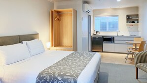 A hotel room with a bed, a wooden wardrobe, a kitchenette with a refrigerator, microwave, and a small dining table with chairs. - Anchorage Motel Apartments (Te Anau)