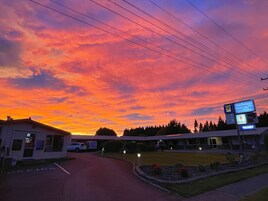 Un motel con un estacionamiento, un cartel indicativo del motel y un cielo al atardecer.
