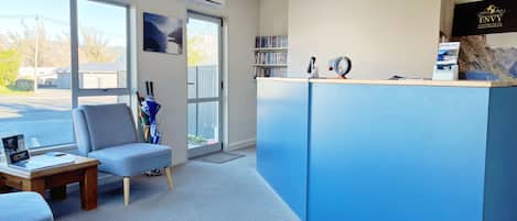 A reception area with a blue counter, a grey armchair, a wooden table, and a bookshelf.