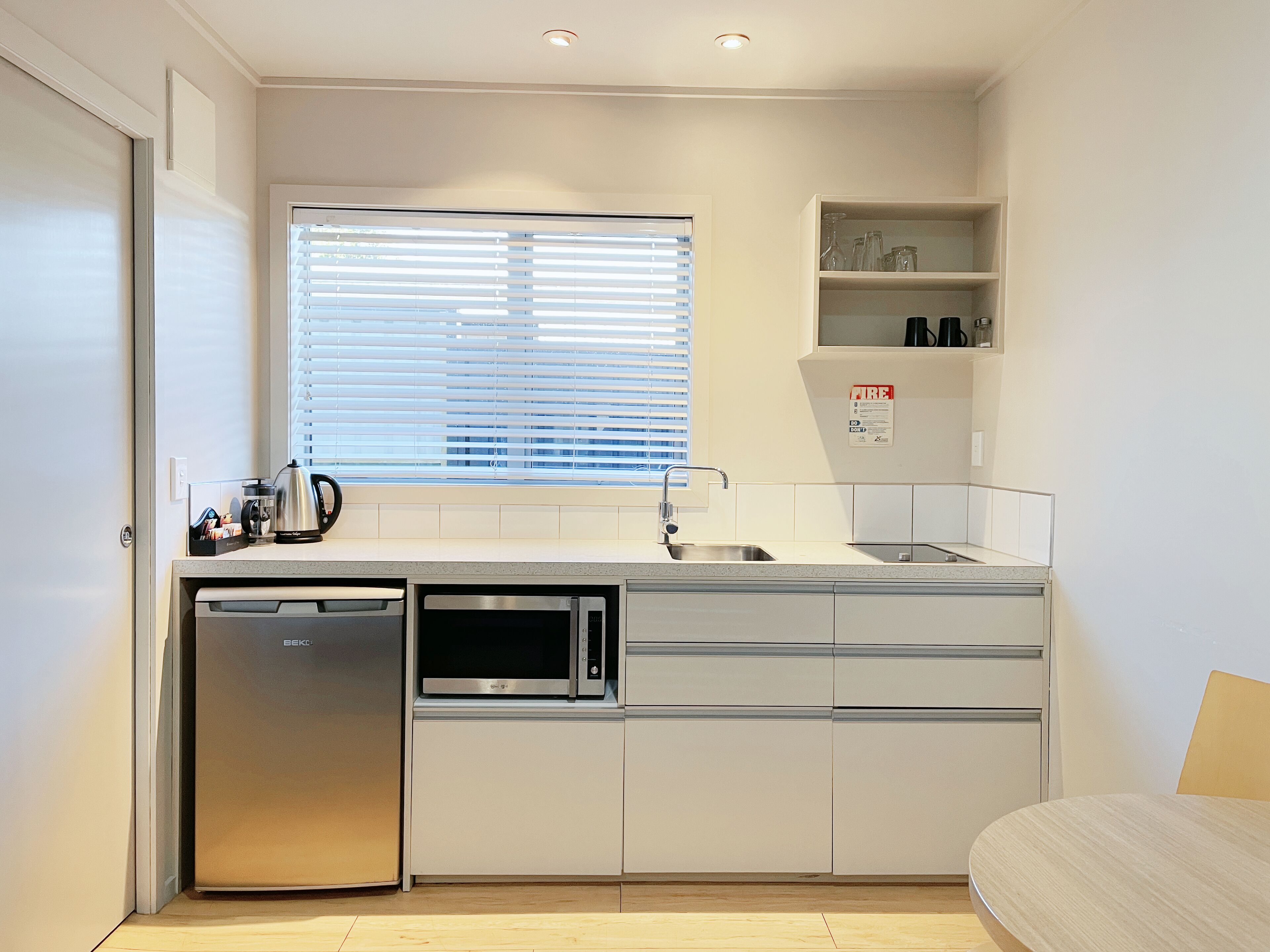 A compact kitchen with a dishwasher, microwave, and a window with blinds.