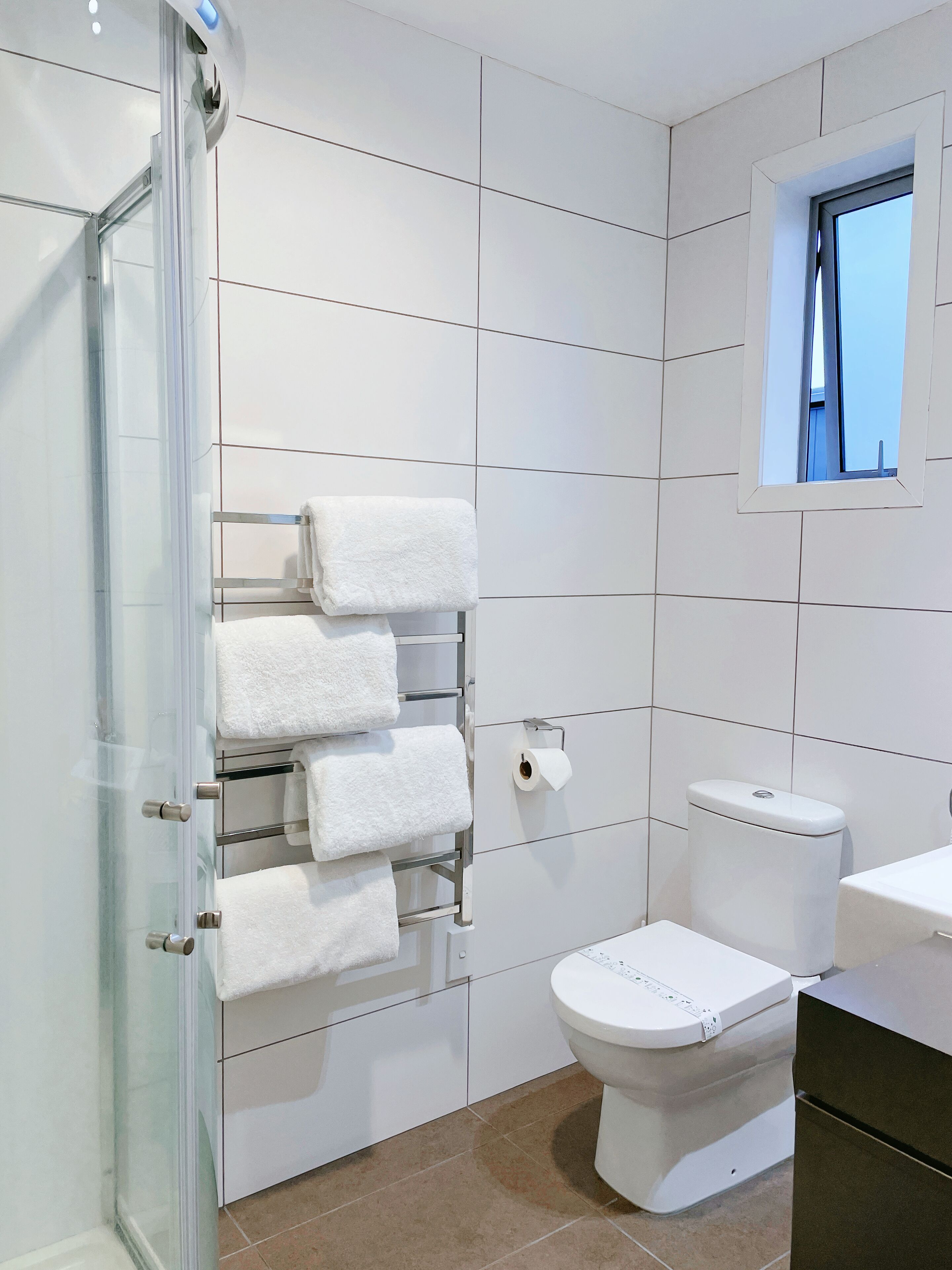 Une salle de bain moderne dotée d’une douche à parois de verre, de toilettes avec panneau de commande et d’un porte-serviettes muni de plusieurs serviettes.