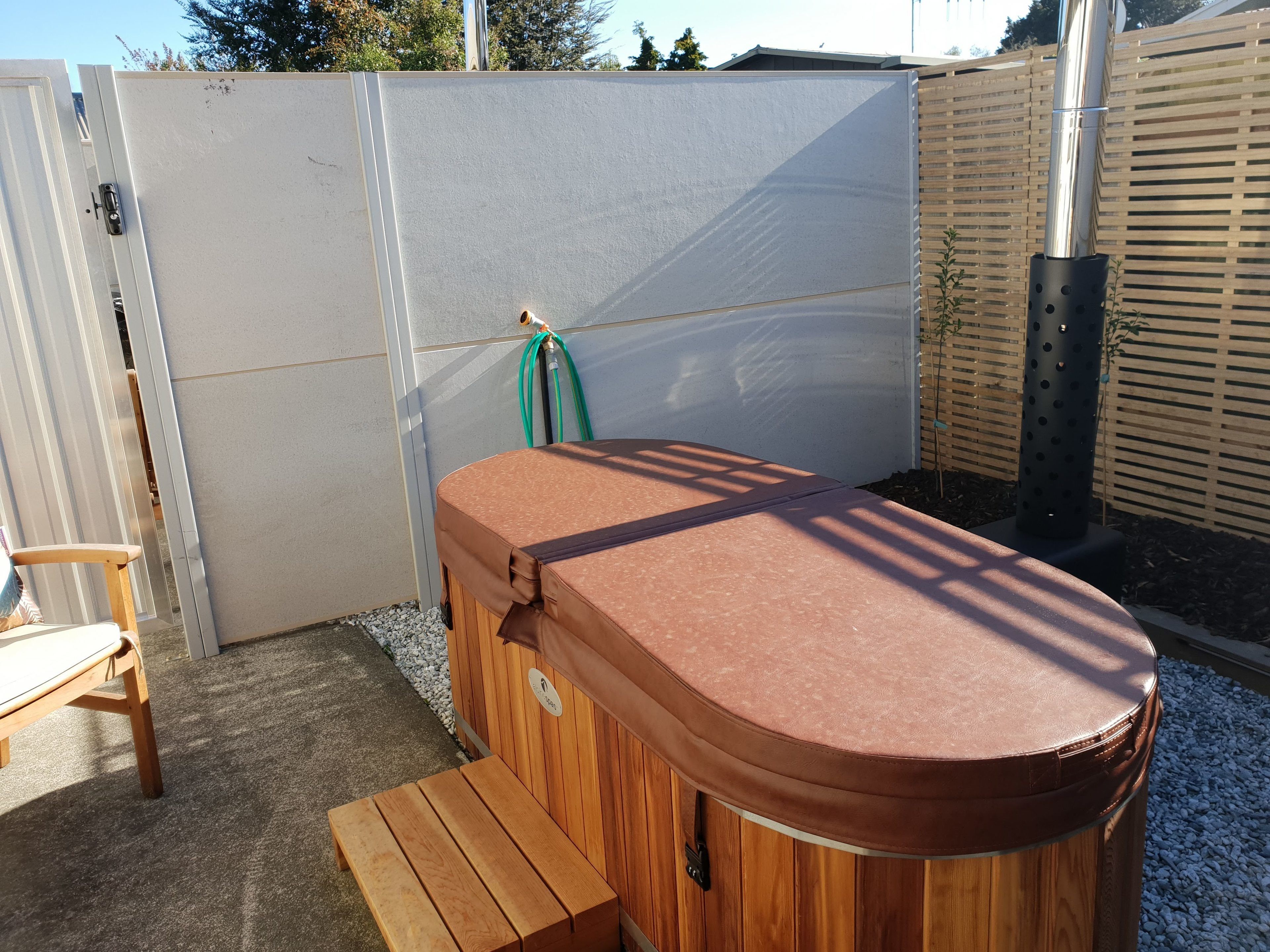 Ein hölzernes Whirlpool mit Sitzbank, einer weißen Tür und einem Holzzaun in einem Garten.