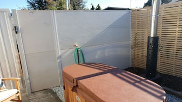 Ein hölzernes Whirlpool mit Sitzbank, einer weißen Tür und einem Holzzaun in einem Garten.
