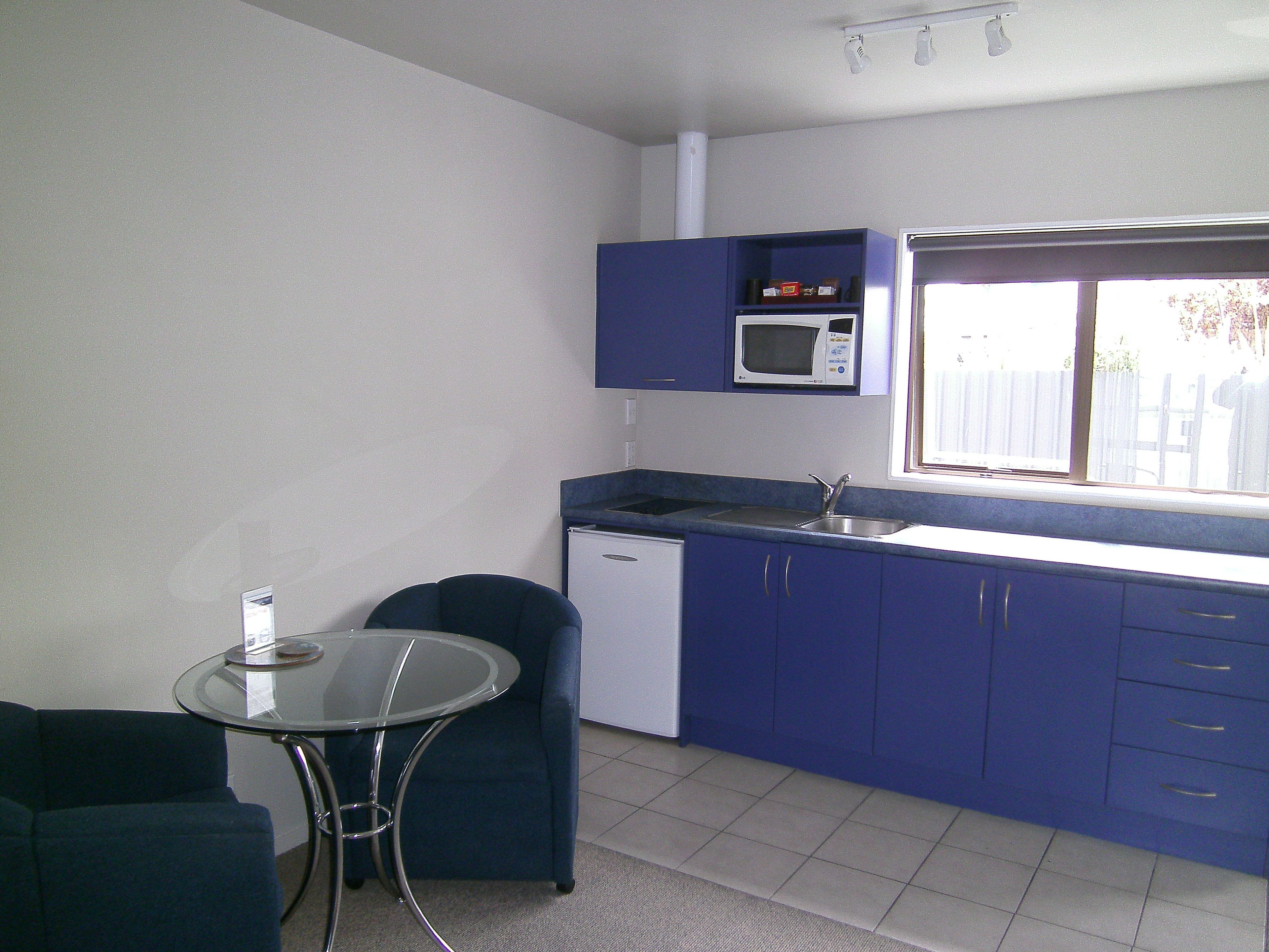 Una cocina compacta con microondas, lavamanos y armarios azules.