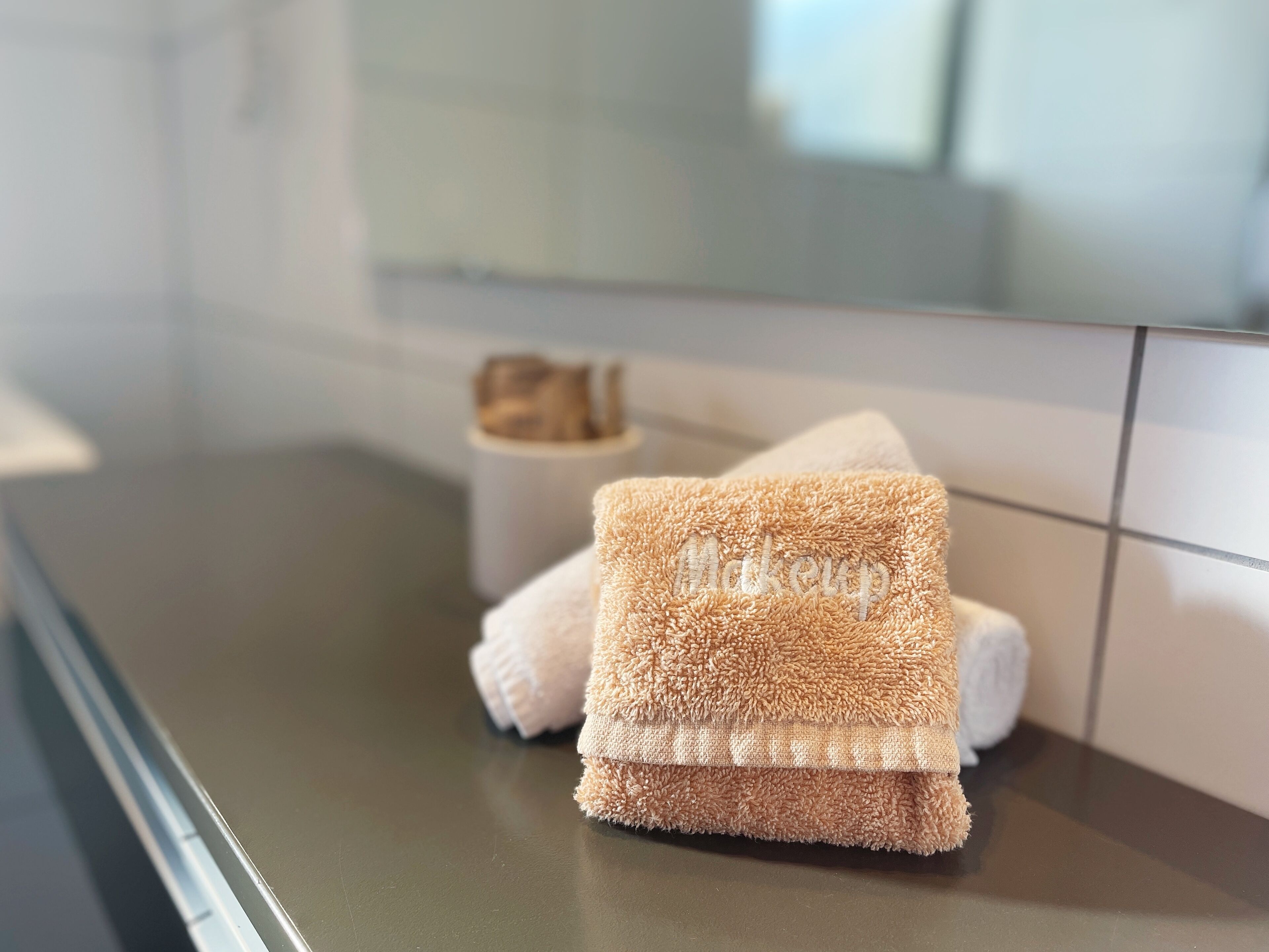 A bathroom with a towel rack holding two towels, one with the word "makeup" embroidered on it.