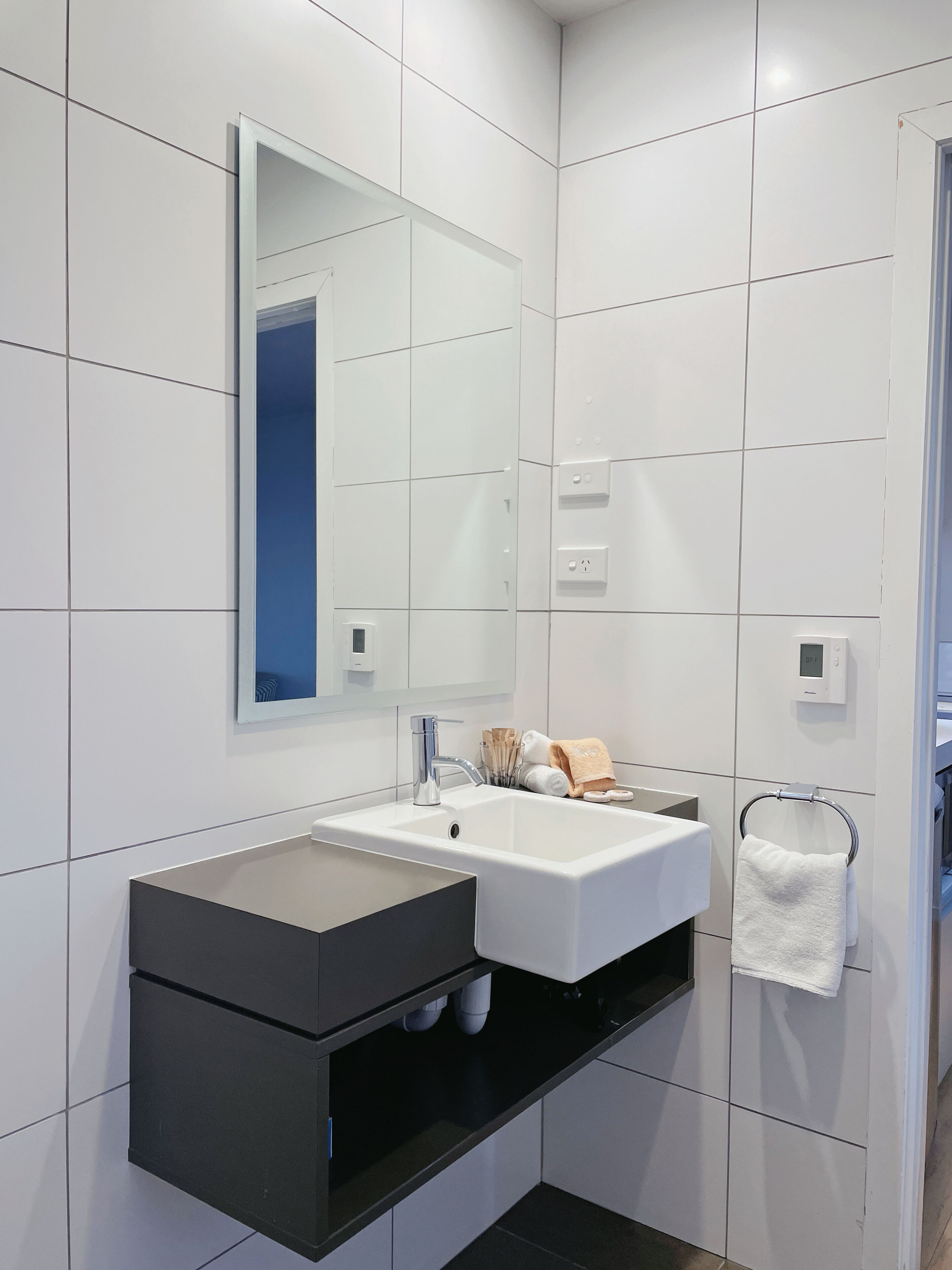 Un baño moderno con un lavamanos, espejo y toallero blancos.