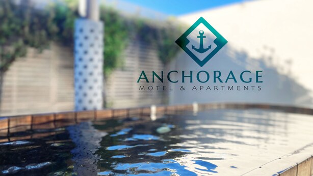 A pool with a wooden edge, surrounded by a wooden fence and greenery. - Anchorage Motel Apartments (Te Anau)