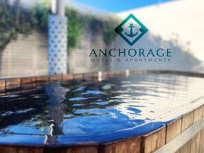 A pool with a wooden edge, surrounded by a wooden fence and greenery. - Anchorage Motel Apartments (Te Anau)