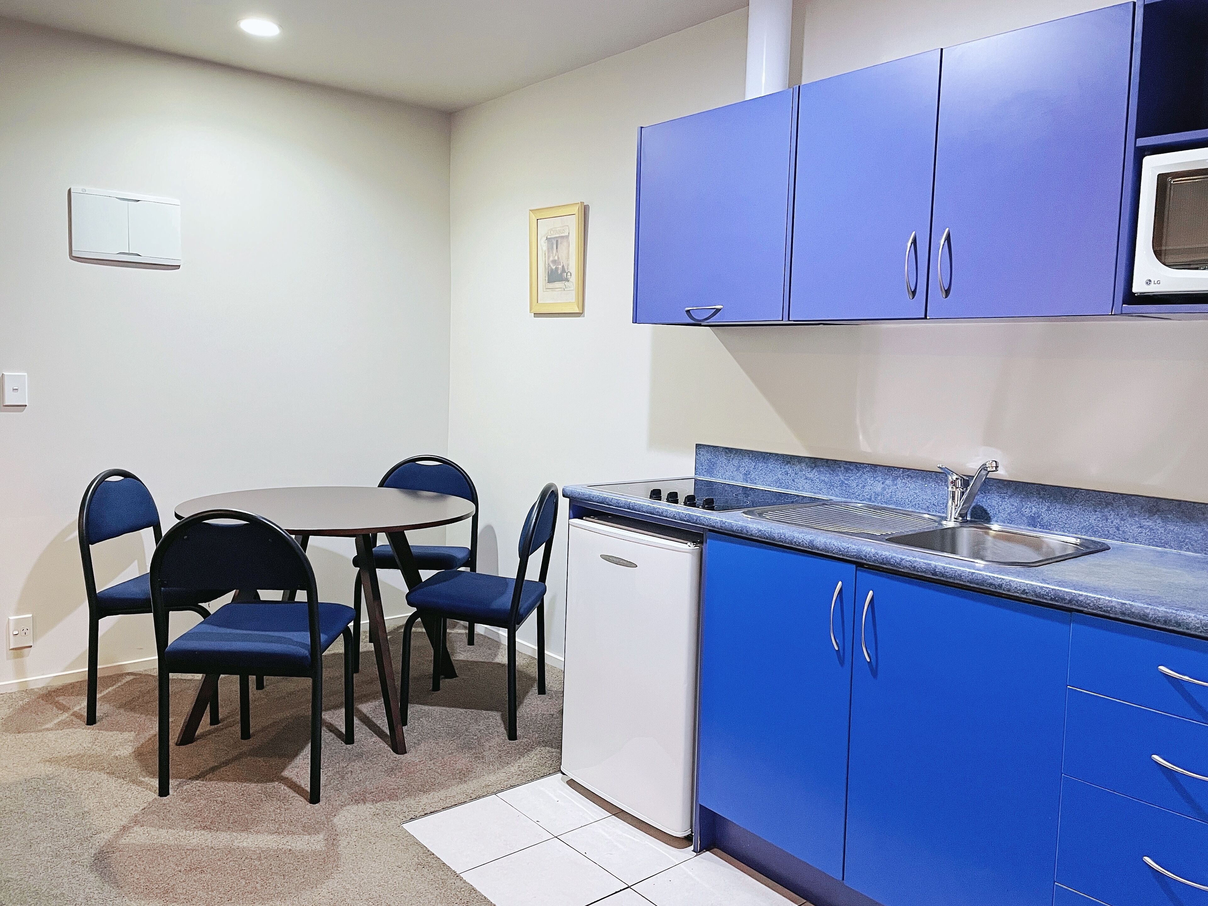A compact kitchen with blue cabinets, a microwave, a sink, and a small dishwasher.