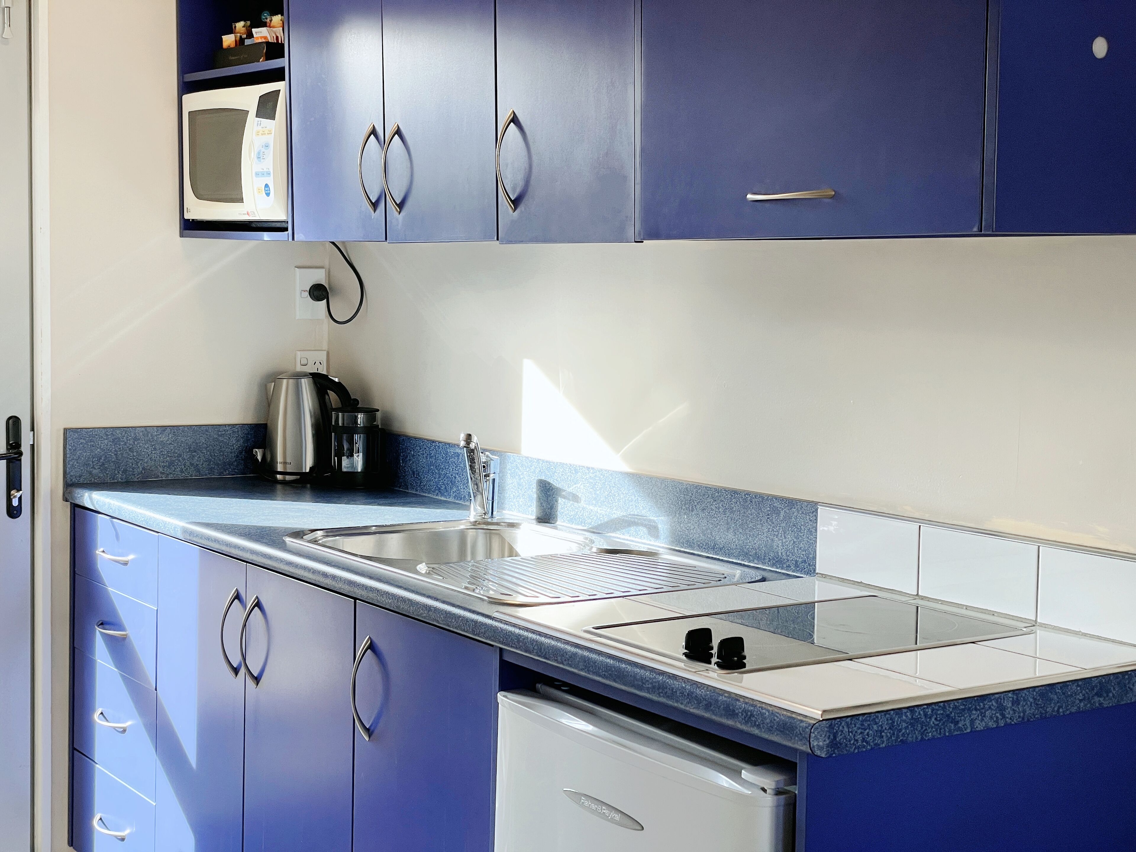 Une cuisine moderne avec des armoires bleues, un évier en acier inoxydable et un four à micro-ondes encastré.