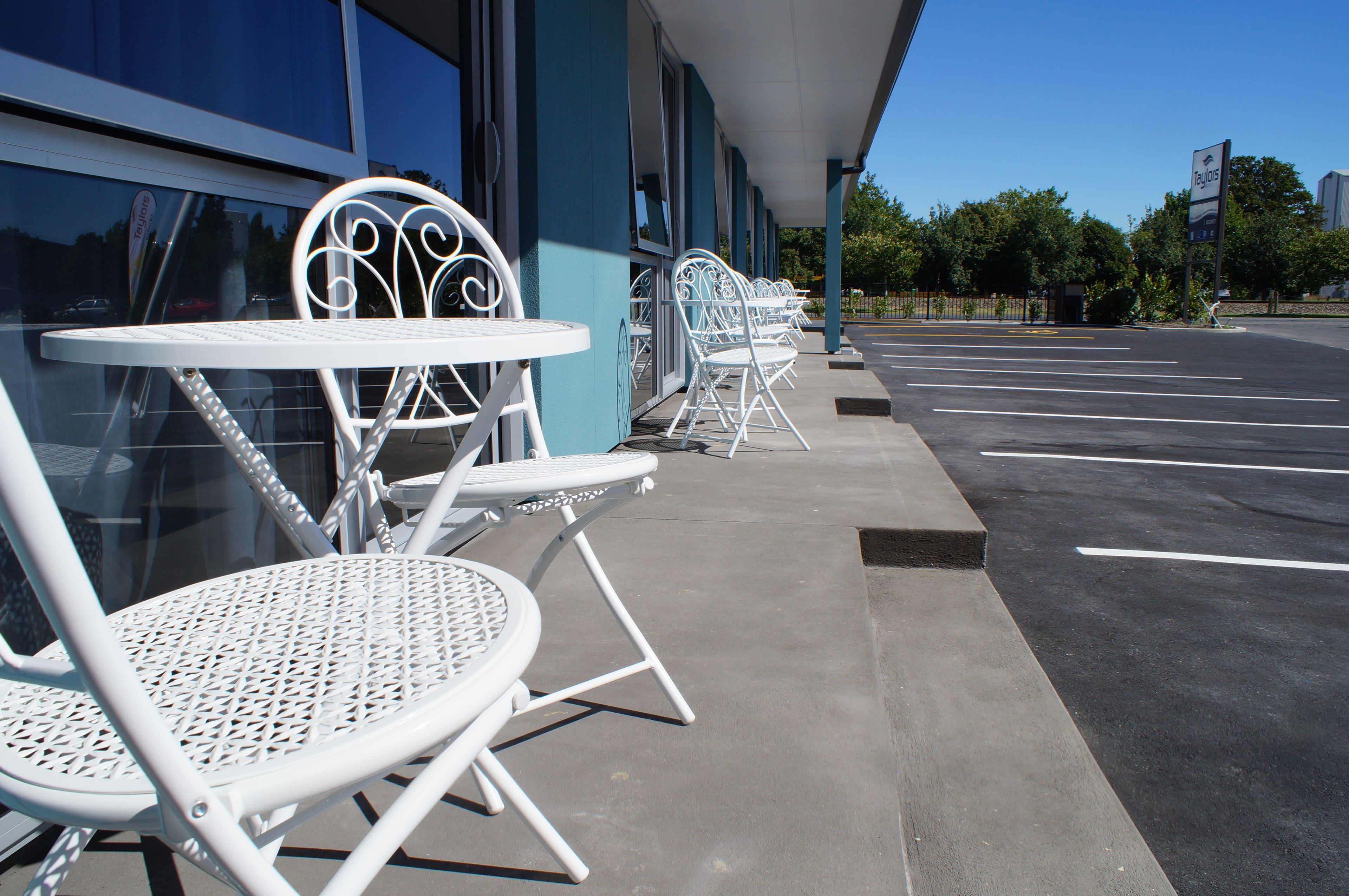 Outdoor seating with tables and chairs, a parking lot, and a building facade.