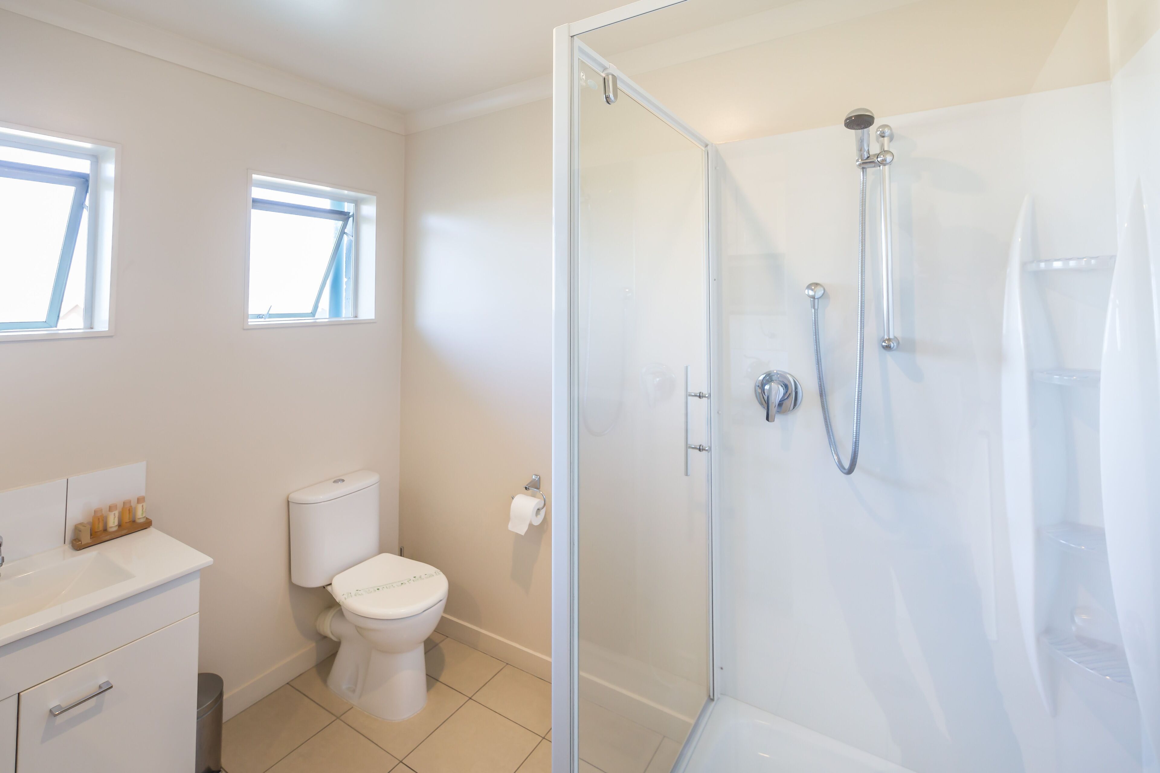 Un baño moderno con ducha envuelta en vidrio, inodoro y lavamanos con espejo.